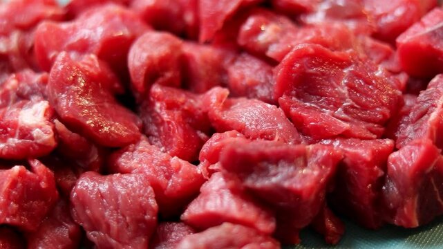 Close up of raw beef meat chopped in small cubes on green cutting board 
