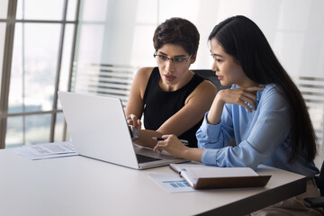 Two multiethnic project managers women talking at laptop, watching Internet startup presentation,...