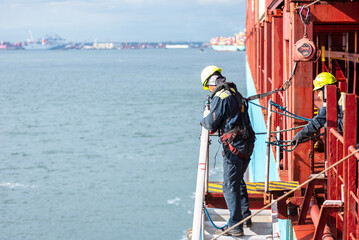 A deckhand prepares the pilot ladder as the ship readies for port entry. Secured in a safety...