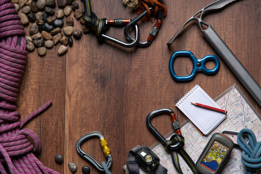 wooden table with climbing equipment, rope, carabiners, ice axe, map, gps, headlamp, pocket knife and notebook