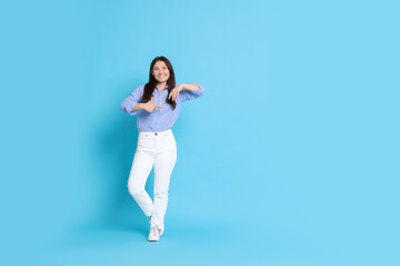 Smiling woman pointing at something on light blue background. Space for text