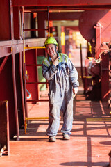 A smiling deck crew member, standing on the deck of a merchant ship in his work gear and helmet. Despite the isolation of life at sea, his expression reflects resilience and positivity.