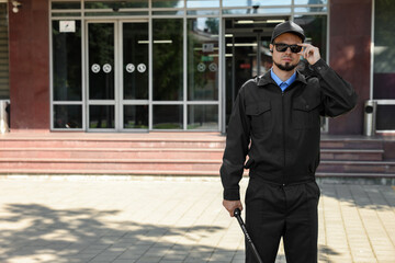 Security guard in uniform and sunglasses with baton outdoors, space for text