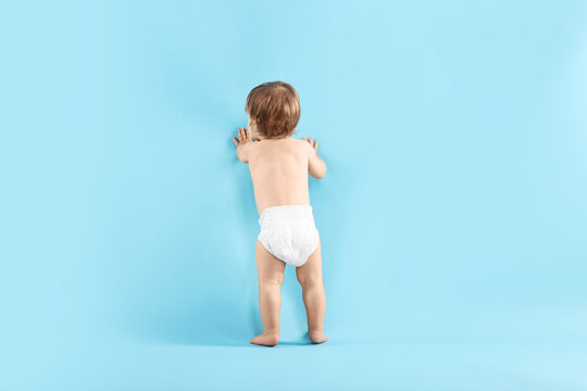 Little child in diaper on light blue background, back view