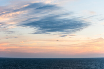 Pastel clouds drift across the sky, the colors blending softly into the horizon. The Atlantic Ocean below lies calm, reflecting the fading light as day gives way to night.