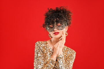 Beautiful young woman with carnival mask on red background