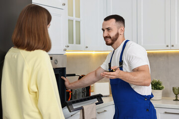Obraz premium Smiling repairman consulting woman near oven in kitchen