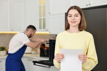 Obraz premium Smiling woman with sheet of paper and repairman fixing oven in kitchen, selective focus