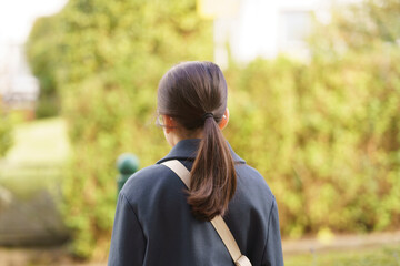 A little girl with a ponytail stands with her back to the camera against a green fence. Concept of...
