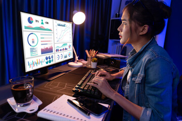 Smiling young beautiful asian creative looking on pc of profit of sales target report and writing on notebook for memo with planning invest new strategy market project at neon light night. Stratagem.