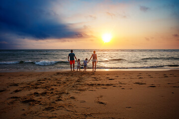 A group of four family members stroll on sandy shore at sunset