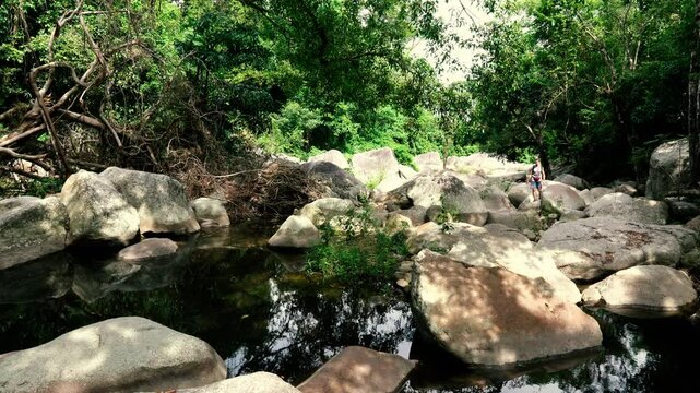 A tourist moves over large boulders in the bed of a mountain river in the jungle