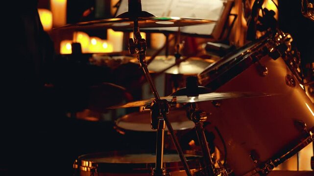 Close-up of a drum kit during a live performance. Drums and cymbals actively played by the drummer. Warm lighting creates an inviting atmosphere, enhancing the concert experience