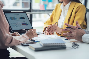 Strategic Business Meeting: Focused team collaboration around a table, reviewing data on a laptop and documents.  Hands actively engaged in discussion and analysis.