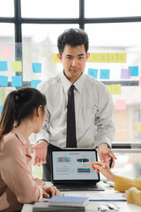 Strategic Presentation: A focused team of business professionals, led by a confident presenter, engages in a productive discussion while reviewing data on a laptop screen.