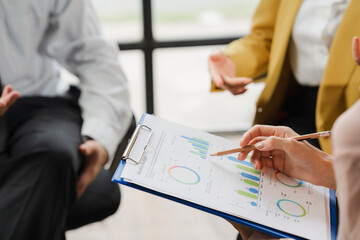Business Meeting Analysis: A close-up shot focusing on hands and a clipboard displaying detailed financial charts and graphs during a business meeting.  The image conveys collaboration.