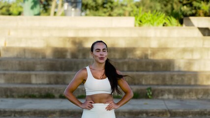 Active woman pausing after workout, hands on hips as catches breath. Determined jogger resting post run, gazing into distance