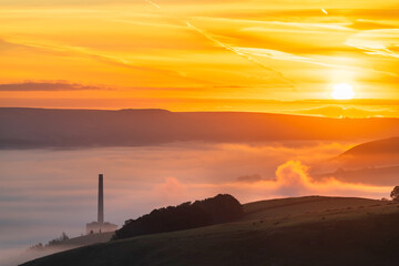 Hope valley at sunrise with cloud inversion and chimney of Cement works factory in Peak District....