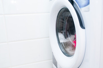 Washing machine with colored clothes and foam inside. Front view, ashing things in the washing machine. Close-up of the front cover of a household appliance