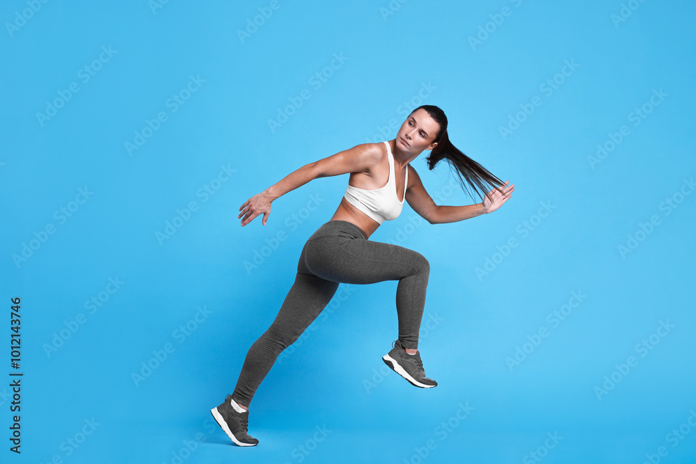 Wall mural Woman in sportswear running on light blue background