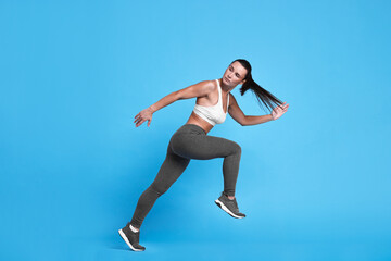 Woman in sportswear running on light blue background