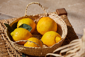 A woven basket filled with fresh lemons on a textured mat, with natural sunlight highlighting the vibrant yellow color and green leaves