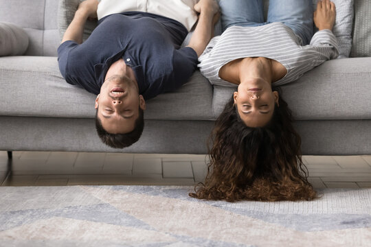 Sleeping young married couple lying upside down on home sofa, having fun, keeping strange funny pose for relaxation on comfortable couch, relaxing with head and hair hanging to floor