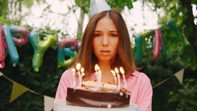 A sad woman with party hat stands alone surrounded by festive birthday decorations, balloons, and flags, feeling disappointed that no one showed up to her party