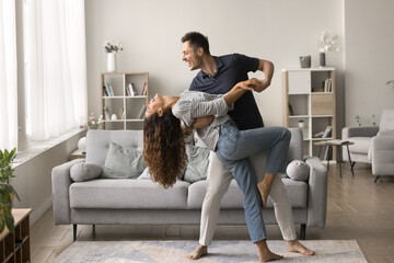 Happy active married couple dancing in stylish living room interior, enjoying activity at home...