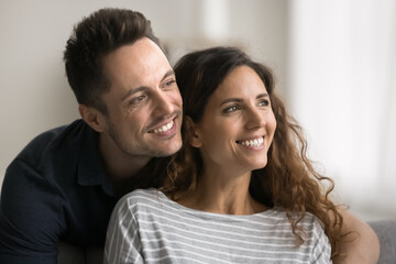 Obraz premium Happy dreamy couple in love sitting close with head touches, looking at window away with toothy smiles, discussing plans, house buying, mortgage, enjoying closeness, good relationship