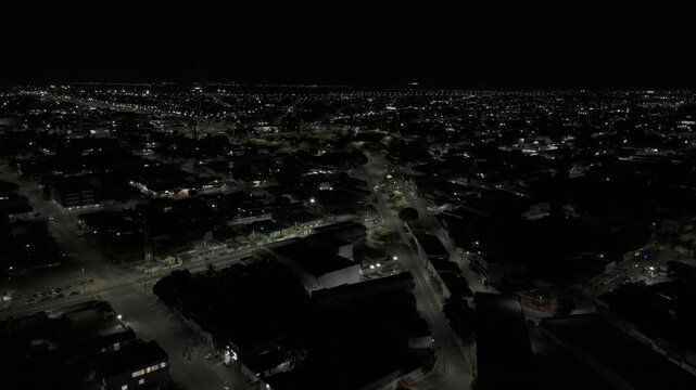 Drone flies over city with no tall buildings lit up at night