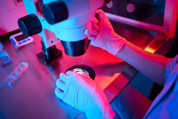 Doctor using a microscope under red and blue lighting
