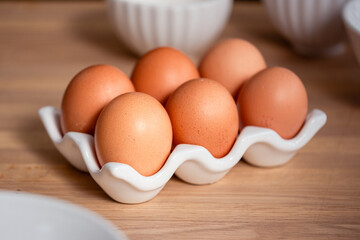 Fresh brown eggs arranged in a white ceramic holder on wooden kitchen table, natural food...