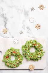 Two wreaths made of green food are on a white cutting board