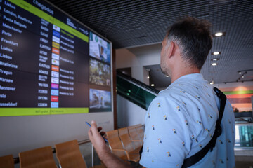 A male traveler with a backpack looks at the information board of departures and arrivals at the airport.