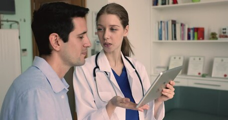 Close up therapist hold tablet review health test results, showing medical images use medical apps access, demonstrate rehabilitation exercises to male patient at visit in hospital. Tech and medicine