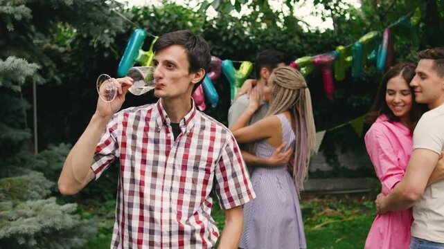 A lonely guy standing at the edge of a birthday party, sipping champagne while couples dance happily around him, highlighting his solitude amidst the celebration