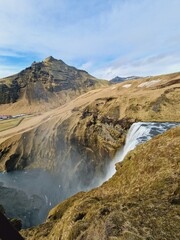 Nordic skgafoss waterfall flowing down hills, creating spectacular arctic scenery near cliffs edge. Massive icelandic cascade falling off of brown slopes, icy landscape in iceland.