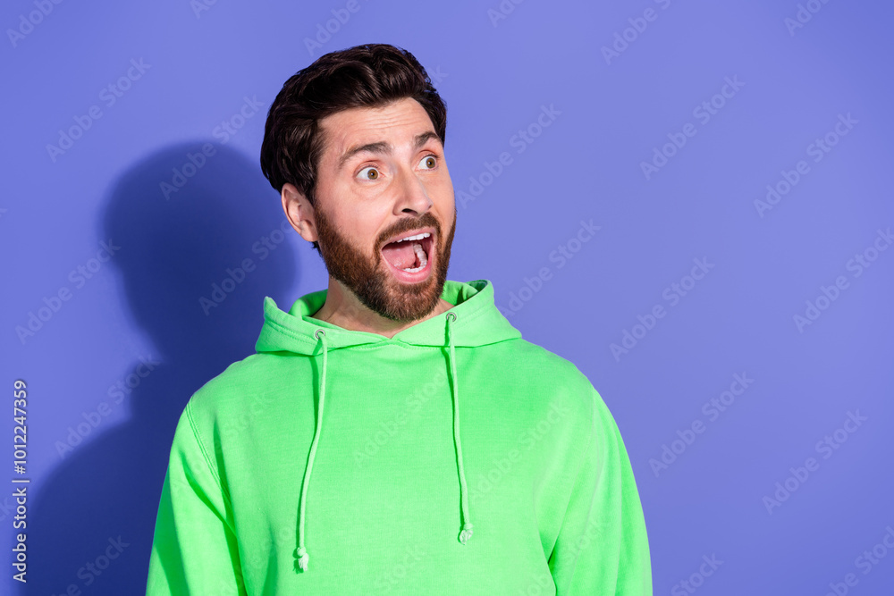 Wall mural Photo portrait of handsome mature age surprised reaction man wearing bright green hoodie sportswear isolated on violet color background