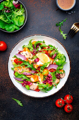 Foodie food salad with baked salmon and tomatoes, cucumber, arugula, radicchio, onion and lettuce with lemon and olive oil dressing.  Brown background, top view