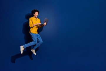 Obraz premium Full size photo of nice young man jump laptop empty space isolated on dark blue color background