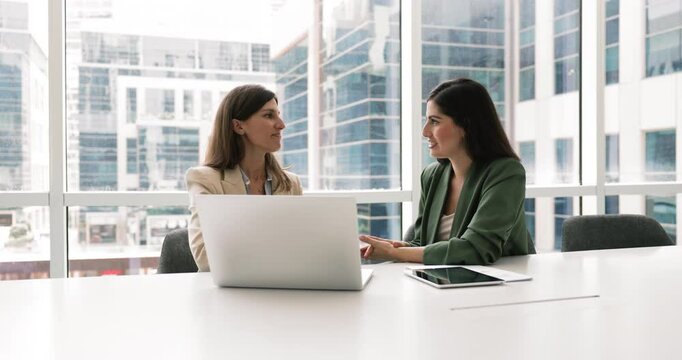 Two businesswomen in boardroom discuss strategic plans for upcoming project, analyze financial reports, evaluating strategy, brainstorm new ideas to improve business processes or recent market trends