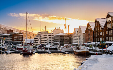 Tromso harbor at sunset in winter, Norway. View of Scandinavian buildings and boats in port of Tromso with mountain in background. Snowy winter landscape in arctic circle town in far northern Norway