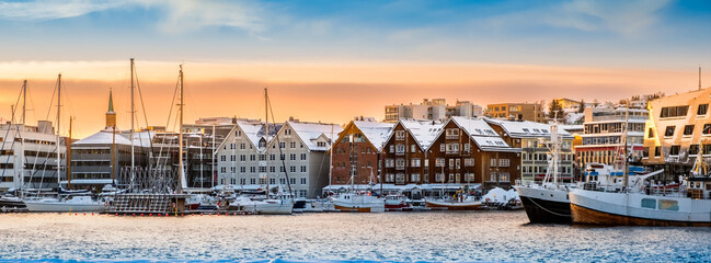 Tromso harbor at sunset in winter, Norway. View of Scandinavian buildings and boats in port of Tromso. Snowy winter landscape in arctic circle town in far northern Norway