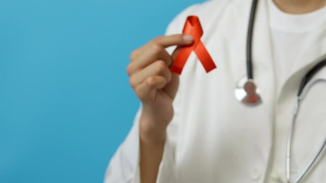 Young male doctor shows a red ribbon, symbol of the fight against VIH/SIDA, against drugs, blue background