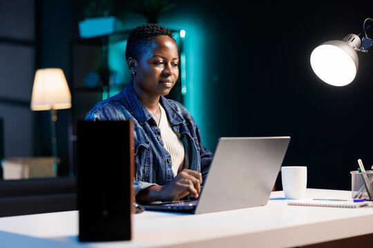 In home office, african american self employed worker typing on laptop and searching the internet for information. Female creative writer sitting at desk using wireless computer, creating content.