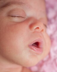 Close-up face of sleeping newborn, baby girl with pink blanket background