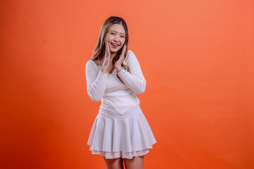 expression of beautiful young girl in white top standing cheerfully to the camera both palms in front of mouth isolated orange background. for fashion, advertising, promotion, commercial