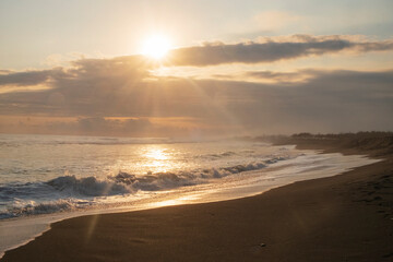 The evening view before sunset on the beach. The sky is orange and the sun is shining brightly. Beautiful black sand coastline
