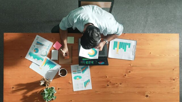 Top aerial view of manager working on laptop while looking at data analysis. Leader compare financial statistic graph while making decision at meeting table with document scatter around. Convocation.